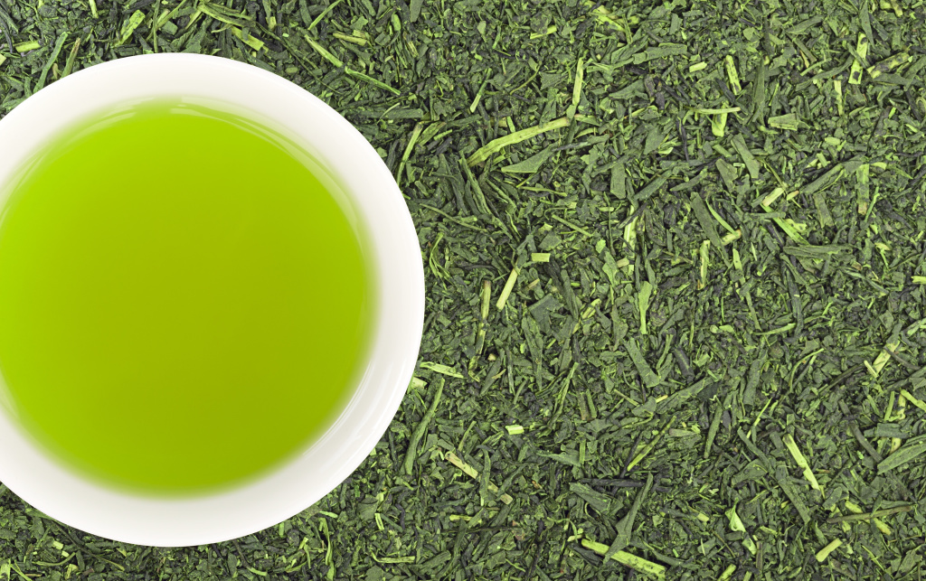 Cup of green tea and green tea leaves background